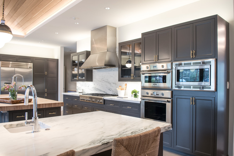 This is an example of a large transitional l-shaped eat-in kitchen in Dallas with a drop-in sink, beaded inset cabinets, grey cabinets, marble benchtops, white splashback, stone slab splashback, stainless steel appliances, limestone floors, with island and beige floor.