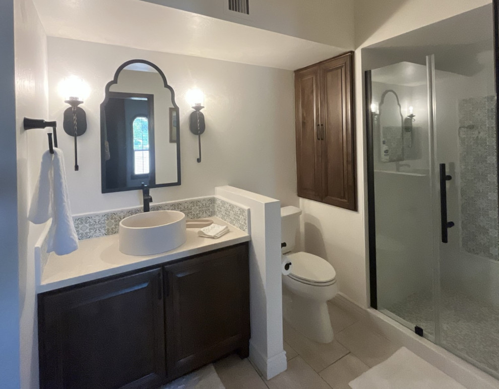 Свежая идея для дизайна: ванная комната среднего размера в стиле неоклассика (современная классика) с фасадами с выступающей филенкой, коричневыми фасадами, душем в нише, белой плиткой, керамической плиткой, белыми стенами, полом из керамической плитки, настольной раковиной, столешницей из известняка, бежевым полом, душем с распашными дверями, бежевой столешницей, тумбой под одну раковину и встроенной тумбой - отличное фото интерьера