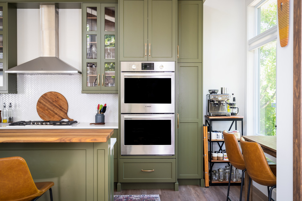 Example of a mid-sized transitional l-shaped medium tone wood floor, brown floor and shiplap ceiling eat-in kitchen design with an undermount sink, shaker cabinets, green cabinets, quartz countertops, white backsplash, ceramic backsplash, stainless steel appliances, an island and white countertops