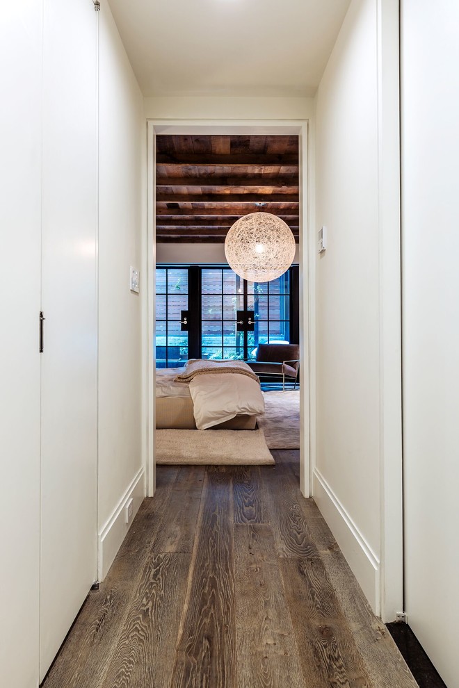 This is an example of a large contemporary master bedroom in New York with white walls, light hardwood floors, a brick fireplace surround, beige floor, exposed beam, brick walls and a two-sided fireplace.