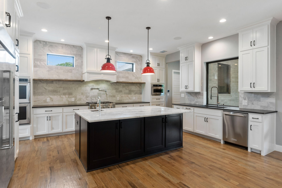 This is an example of a large contemporary u-shaped open plan kitchen in Dallas with an undermount sink, recessed-panel cabinets, white cabinets, granite benchtops, grey splashback, engineered quartz splashback, stainless steel appliances, medium hardwood floors, with island, brown floor and black benchtop.