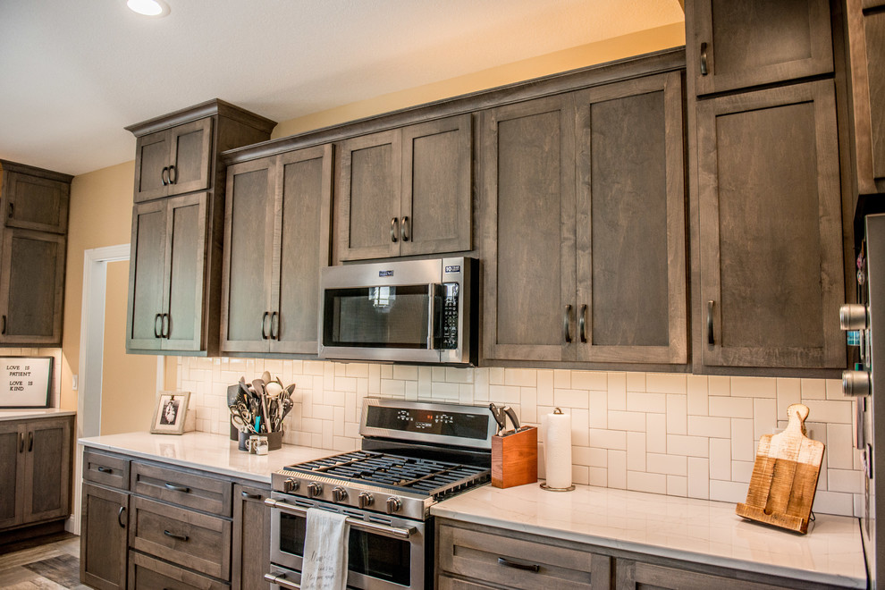 Large transitional l-shaped vinyl floor and multicolored floor open concept kitchen photo with a farmhouse sink, shaker cabinets, gray cabinets, quartz countertops, white backsplash, subway tile backsplash, stainless steel appliances, an island and white countertops