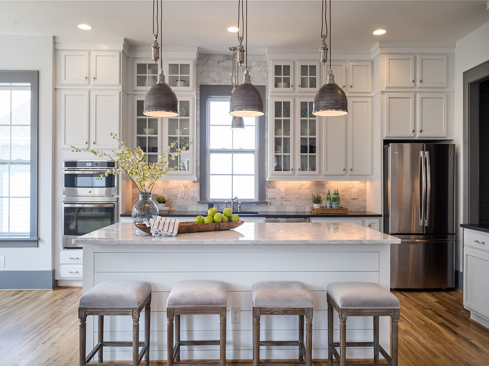 Kitchen - traditional medium tone wood floor kitchen idea in Charlotte with an undermount sink, glass-front cabinets, white cabinets, white backsplash, stainless steel appliances, an island and marble countertops