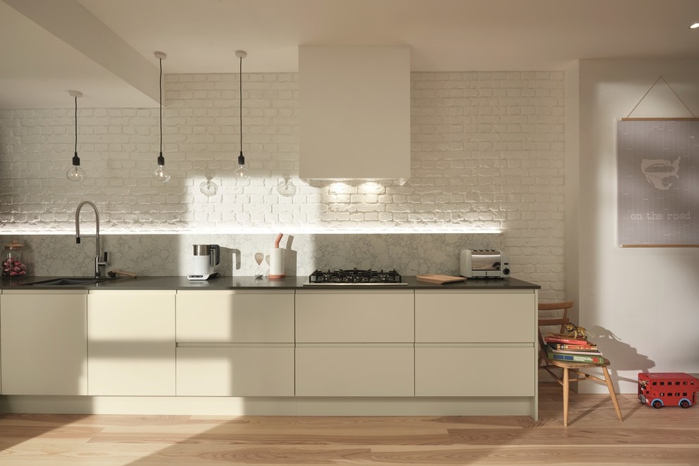 Design ideas for a mid-sized single-wall open plan kitchen in Dublin with an integrated sink, flat-panel cabinets, black cabinets, quartzite benchtops, white splashback, marble splashback, coloured appliances, laminate floors, no island and brown floor.