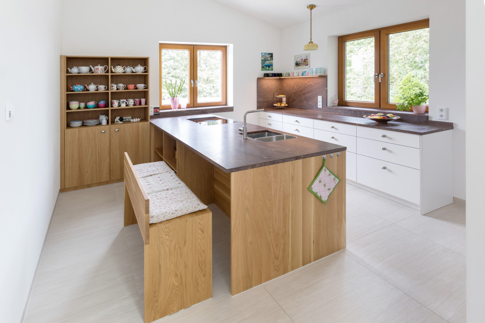 Large contemporary galley open plan kitchen in Stuttgart with an integrated sink, flat-panel cabinets, white cabinets, granite worktops, black appliances, an island and brown worktops.