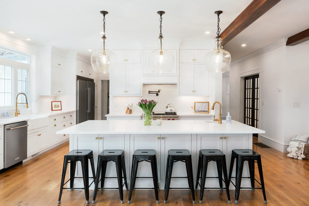 Expansive beach style l-shaped eat-in kitchen in Boston with a farmhouse sink, recessed-panel cabinets, white cabinets, quartz benchtops, with island, white benchtop and white splashback.