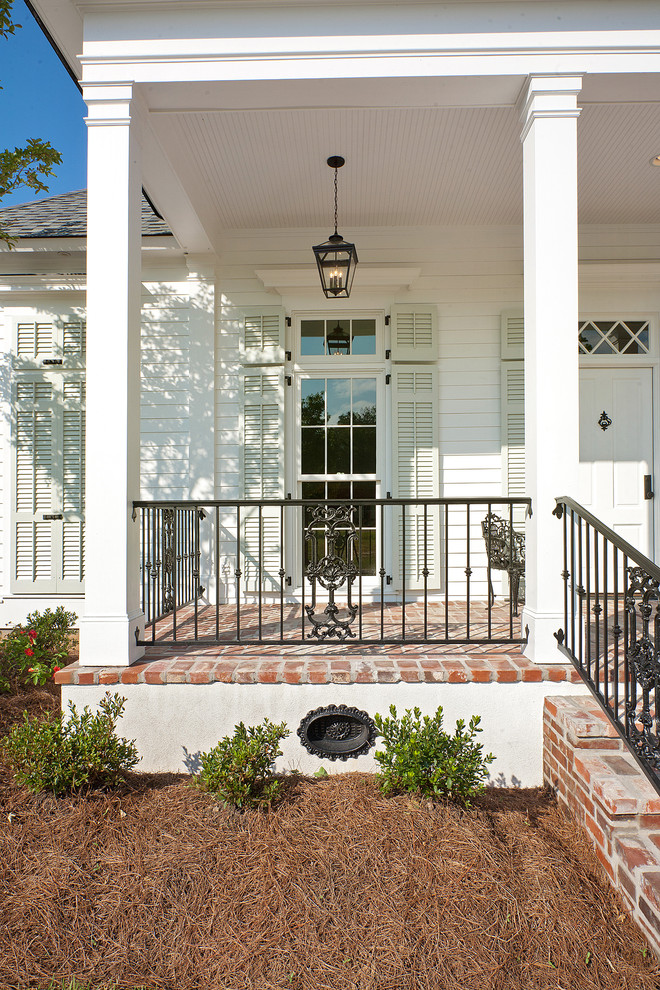 Traditional front yard verandah in New Orleans with brick pavers and a roof extension.