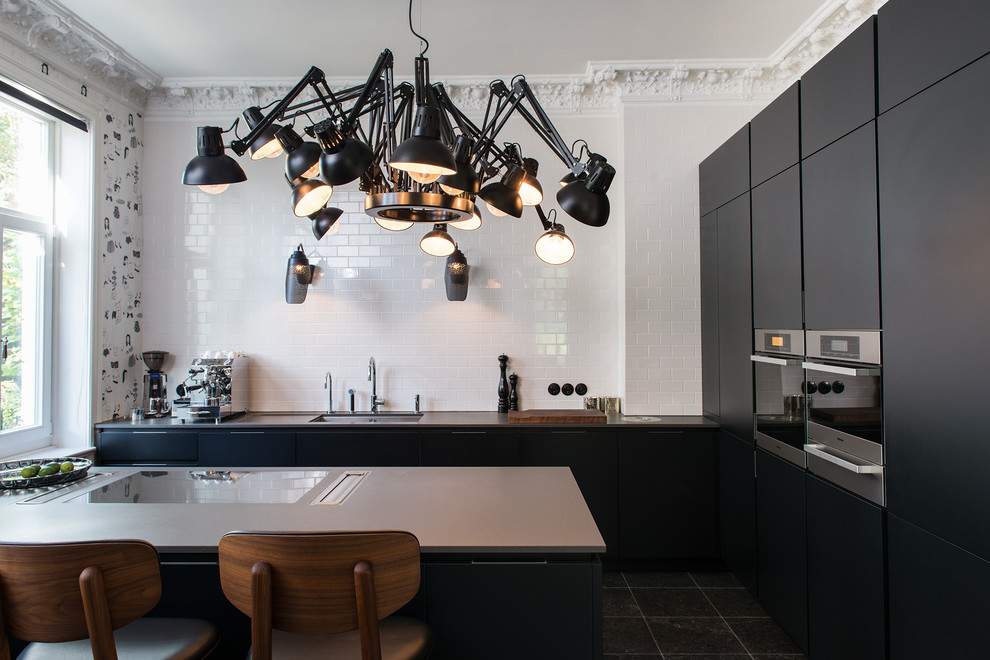 Mid-sized contemporary l-shaped kitchen in Hamburg with an undermount sink, flat-panel cabinets, black cabinets, white splashback, subway tile splashback, panelled appliances, a peninsula and marble floors.