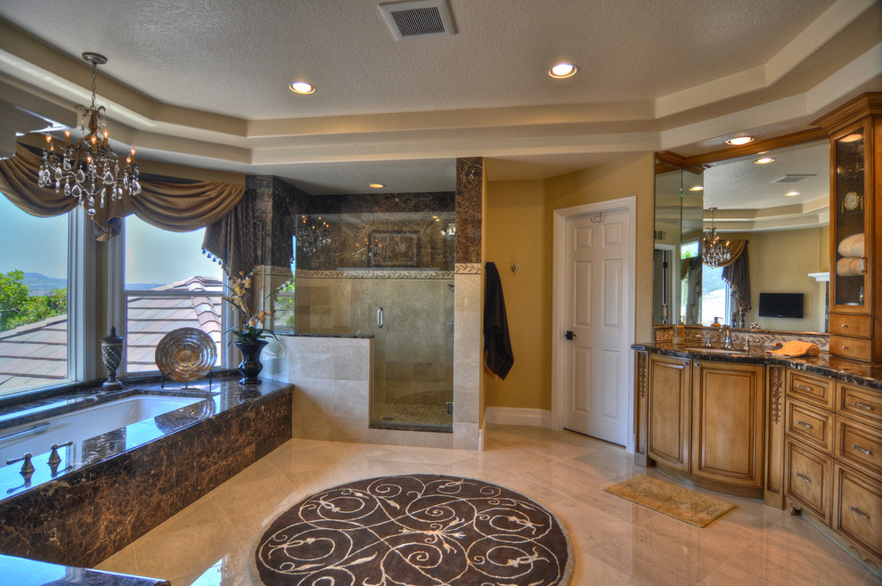 Inspiration for a mediterranean master bathroom in Orange County with an undermount sink, furniture-like cabinets, medium wood cabinets, marble benchtops, an undermount tub, an alcove shower, brown tile, stone tile, beige walls and marble floors.