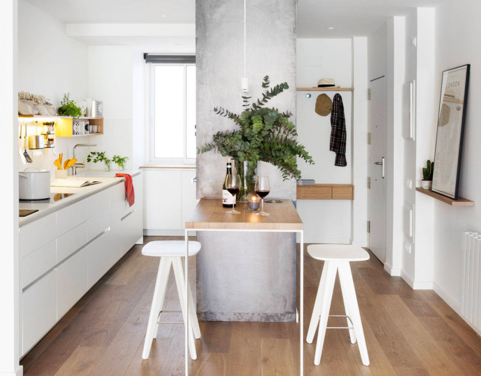 This is an example of a contemporary galley kitchen in Bologna with an undermount sink, flat-panel cabinets, white cabinets, medium hardwood floors, a peninsula, brown floor and white benchtop.