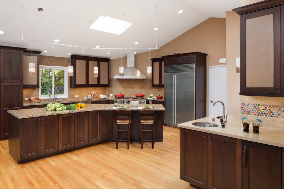 Inspiration for a transitional l-shaped light wood floor open concept kitchen remodel in San Francisco with an undermount sink, recessed-panel cabinets, dark wood cabinets, quartz countertops, beige backsplash, stone tile backsplash, stainless steel appliances and an island