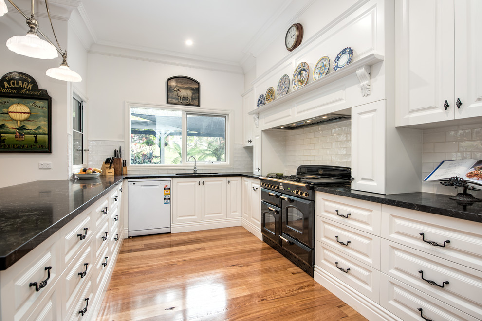Country u-shaped open plan kitchen in Other with an undermount sink, raised-panel cabinets, white cabinets, subway tile splashback, black appliances and a peninsula.