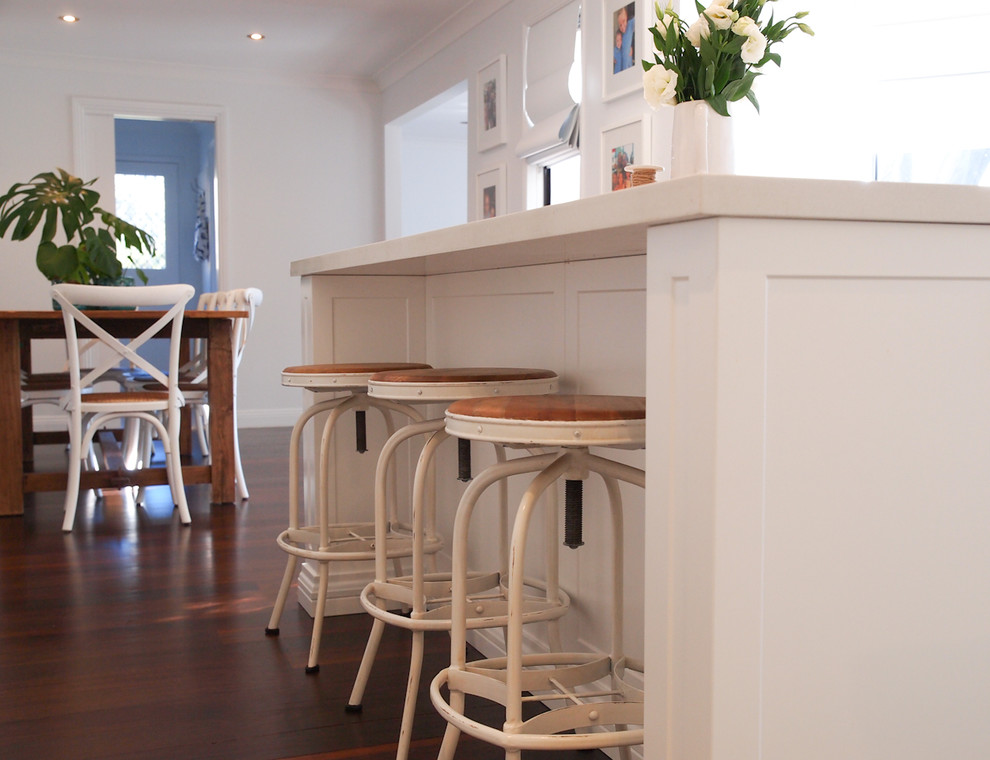 This is an example of a mid-sized traditional kitchen in Wollongong with a farmhouse sink, shaker cabinets, white cabinets, quartz benchtops, white splashback, subway tile splashback, stainless steel appliances, dark hardwood floors and with island.