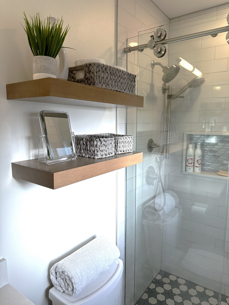 Пример оригинального дизайна: маленькая ванная комната в стиле неоклассика (современная классика) с фасадами в стиле шейкер, фасадами цвета дерева среднего тона, душем в нише, унитазом-моноблоком, белой плиткой, керамической плиткой, белыми стенами, полом из керамогранита, душевой кабиной, врезной раковиной, столешницей из искусственного кварца, серым полом, душем с раздвижными дверями, белой столешницей, нишей, тумбой под одну раковину и встроенной тумбой для на участке и в саду