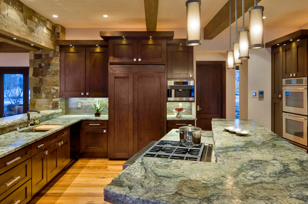This is an example of a country u-shaped kitchen in Denver with recessed-panel cabinets, dark wood cabinets, stainless steel appliances, with island, an undermount sink, granite benchtops, grey splashback, stone tile splashback and medium hardwood floors.
