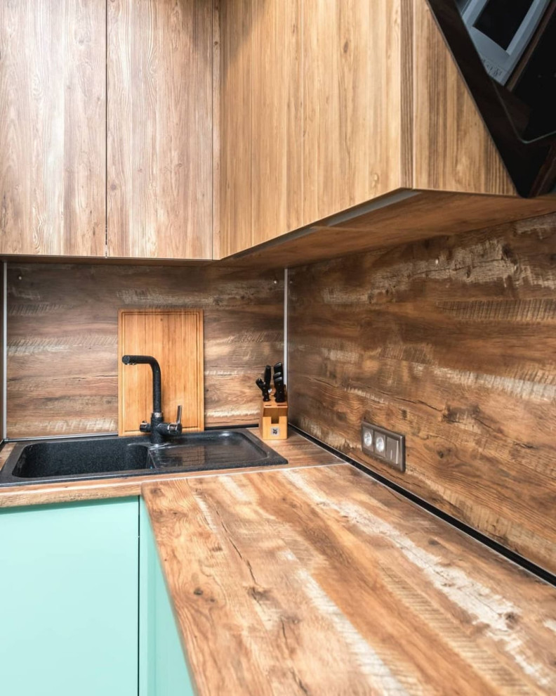 Minimalistisk inredning av ett litet brun brunt kök, med en nedsänkt diskho, släta luckor, turkosa skåp, träbänkskiva, brunt stänkskydd, stänkskydd i trä, svarta vitvaror, linoleumgolv och brunt golv
