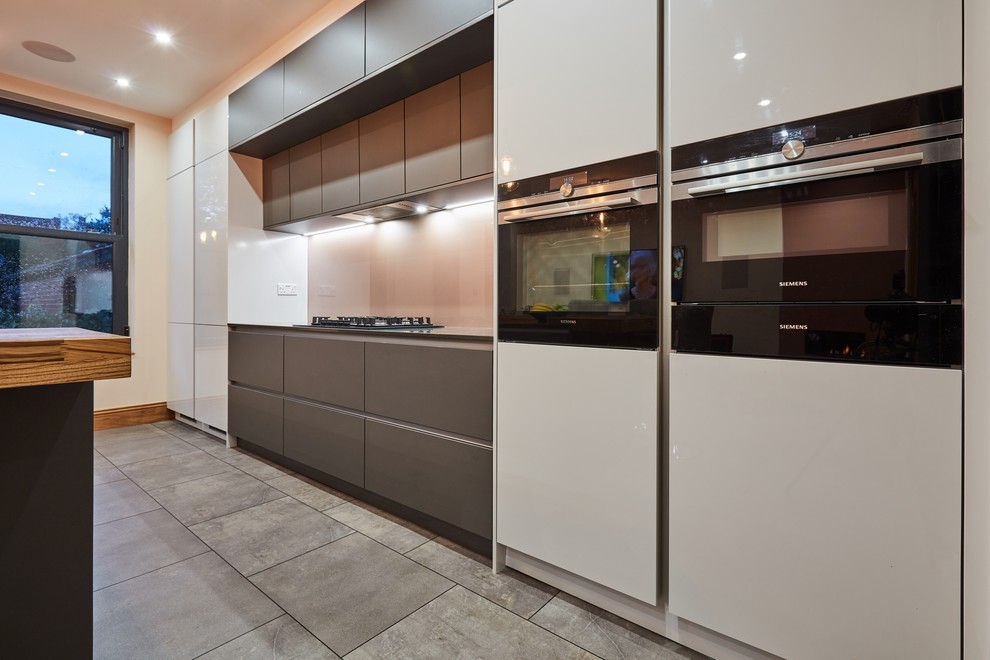 Photo of a mid-sized modern single-wall eat-in kitchen in Other with a drop-in sink, flat-panel cabinets, grey cabinets, quartzite benchtops, metallic splashback, glass sheet splashback, stainless steel appliances, ceramic floors, with island, grey floor and grey benchtop.