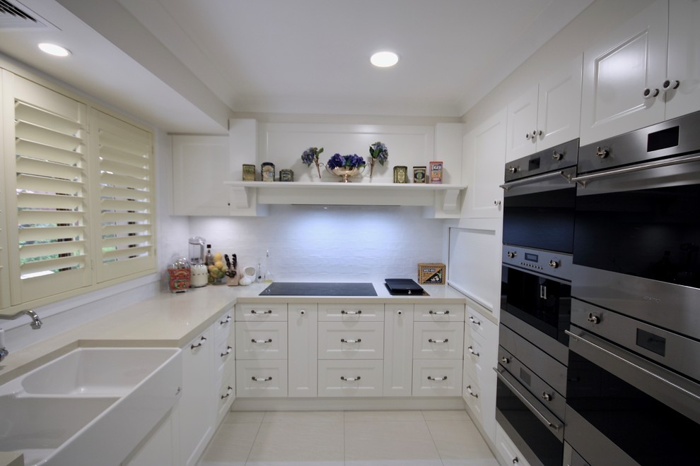 Large traditional u-shaped open plan kitchen in Sydney with a farmhouse sink, recessed-panel cabinets, white cabinets, quartz benchtops, white splashback, subway tile splashback, stainless steel appliances, ceramic floors, with island, beige floor and beige benchtop.