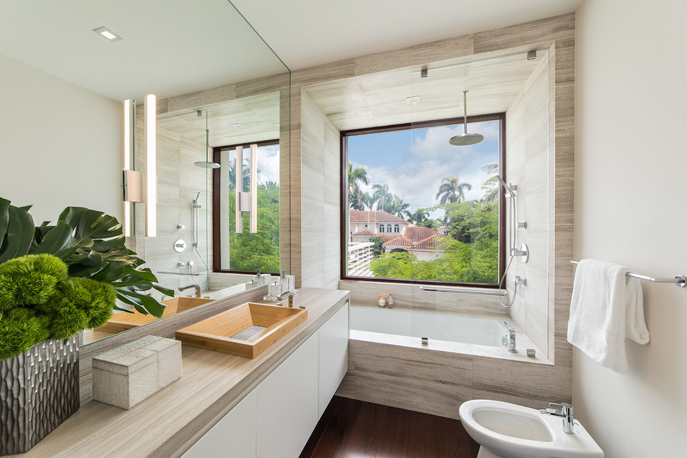 This is an example of a mid-sized beach style bathroom in Miami with flat-panel cabinets, white cabinets, an undermount tub, an open shower, a bidet, gray tile, marble, white walls, dark hardwood floors, an integrated sink, engineered quartz benchtops, brown floor, an open shower and white benchtops.