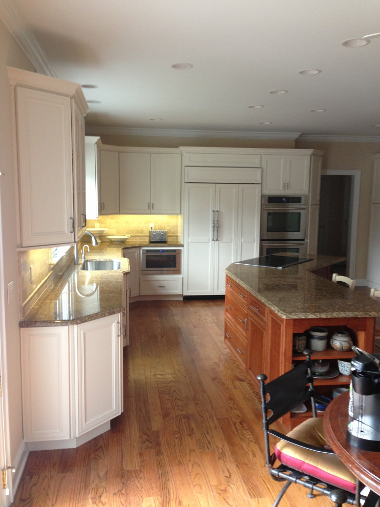 Inspiration for a large transitional u-shaped medium tone wood floor and brown floor eat-in kitchen remodel in New York with an undermount sink, shaker cabinets, white cabinets, granite countertops, white backsplash, porcelain backsplash, stainless steel appliances, an island and multicolored countertops