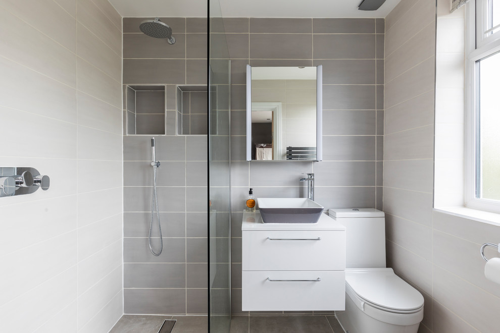 This is an example of a mid-sized contemporary 3/4 wet room bathroom in London with flat-panel cabinets, white cabinets, gray tile, porcelain tile, grey walls, porcelain floors, a vessel sink, solid surface benchtops, grey floor, an open shower and a two-piece toilet.