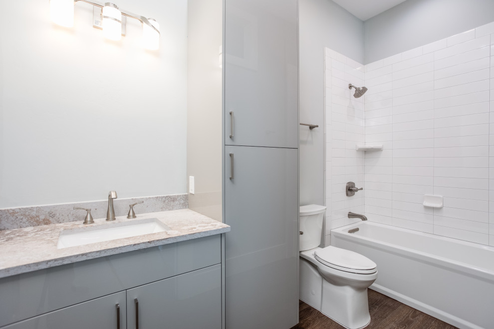 Mid-sized contemporary kids bathroom in Austin with flat-panel cabinets, grey cabinets, an alcove tub, a two-piece toilet, white tile, ceramic tile, grey walls, vinyl floors, an undermount sink, solid surface benchtops, brown floor, multi-coloured benchtops, a single vanity and a built-in vanity.
