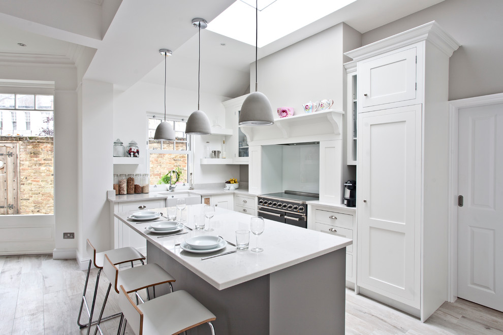Design ideas for a large transitional l-shaped eat-in kitchen in Surrey with a farmhouse sink, shaker cabinets, grey cabinets, solid surface benchtops, grey splashback, glass sheet splashback, stainless steel appliances, light hardwood floors and with island.