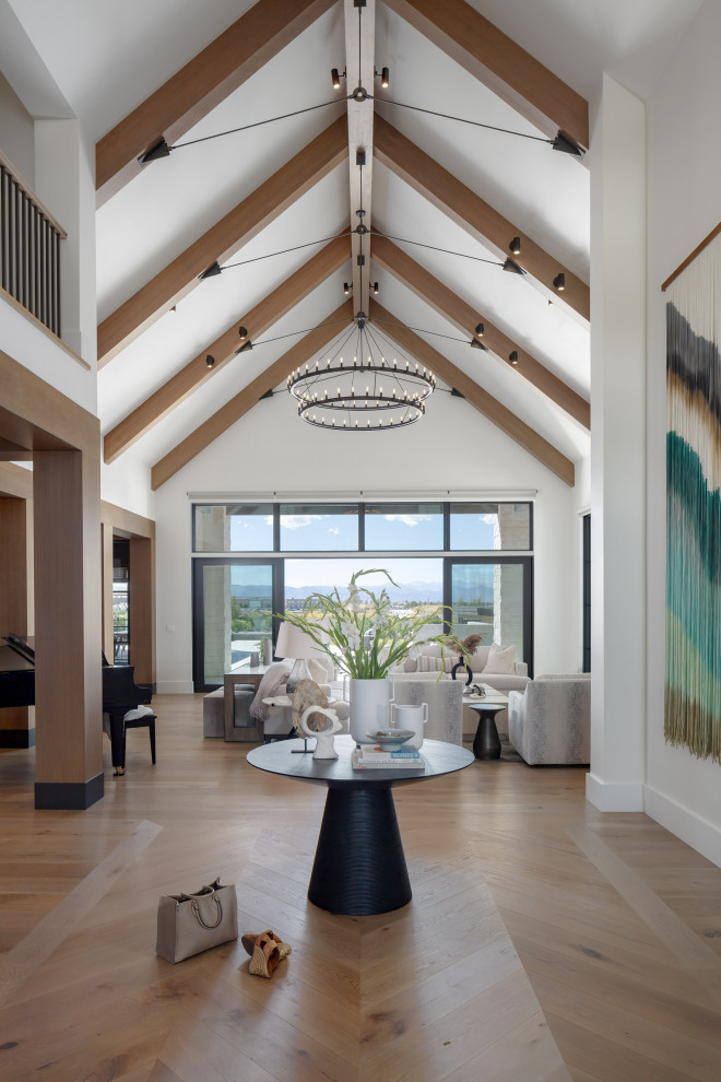 Luxury Custom Home Grand Entryway Foyer Design - The entry of this luxury custom home is stunning with two-story ceilings, exposed beams, herringbone wood floors, oversized chandelier, and bespoke artwork. The eye is drawn up and out the large sliding glass doors to see the stunning mountain views.