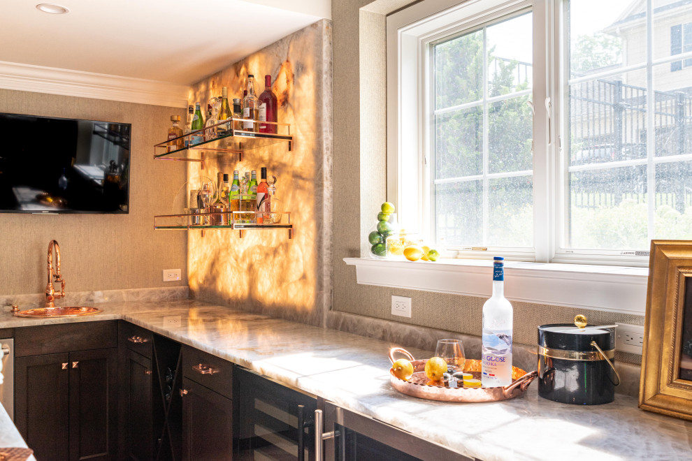 Photo of a large transitional u-shaped wet bar in Philadelphia with a drop-in sink, beaded inset cabinets, brown cabinets, quartzite benchtops, beige splashback, stone slab splashback, porcelain floors, brown floor and white benchtop.