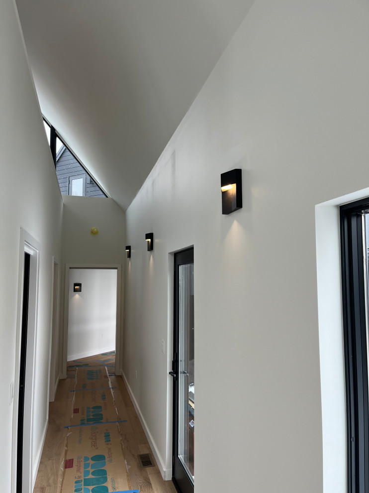Imagen de recibidores y pasillos abovedados modernos con paredes blancas, suelo laminado y suelo marrón
