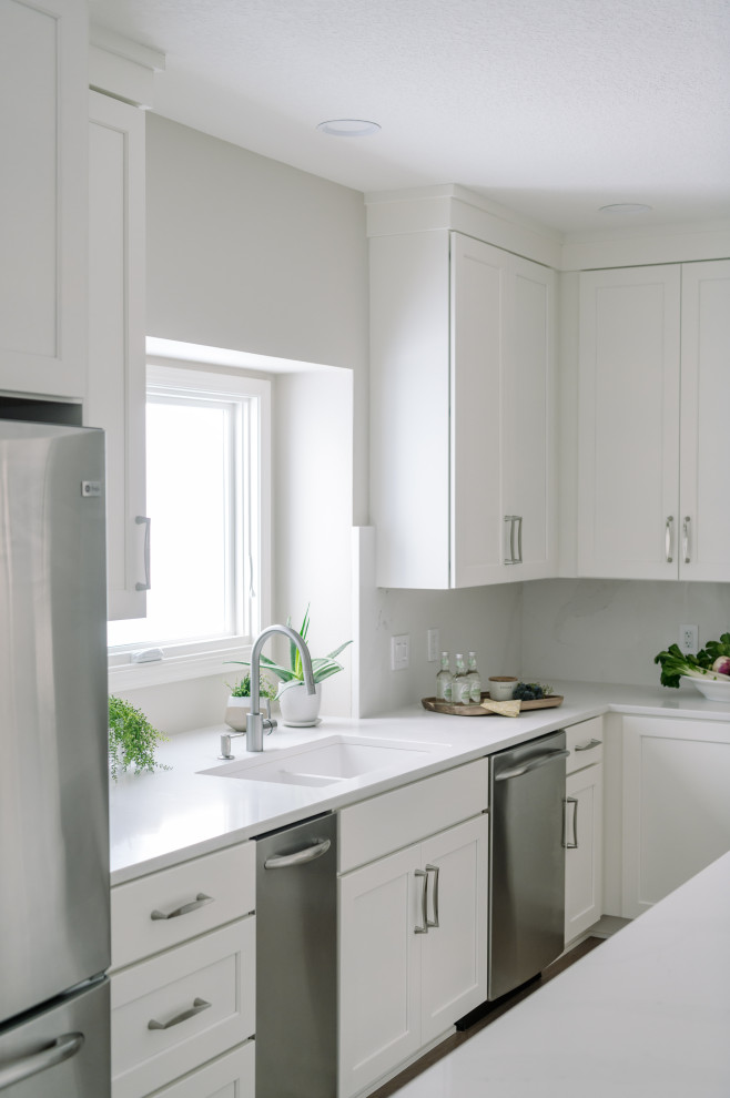 Eat-in kitchen - large transitional l-shaped laminate floor and brown floor eat-in kitchen idea with an undermount sink, shaker cabinets, white cabinets, quartz countertops, white backsplash, quartz backsplash, stainless steel appliances, an island and white countertops