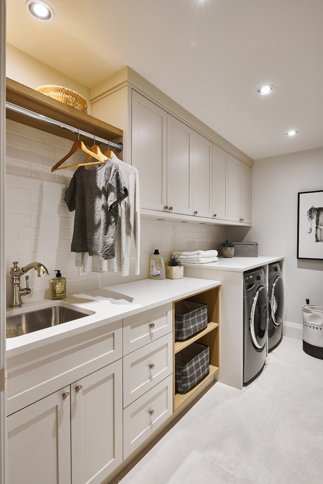 Photo of a large transitional dedicated laundry room in Vancouver with an undermount sink, shaker cabinets, grey cabinets, quartzite benchtops, white walls, porcelain floors, a side-by-side washer and dryer, white benchtop and grey floor.