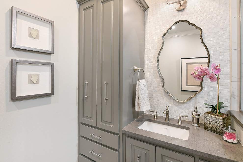 Corner shower - mid-sized transitional 3/4 white tile and marble tile ceramic tile, white floor, single-sink and wallpaper corner shower idea with raised-panel cabinets, gray cabinets, a one-piece toilet, white walls, an undermount sink, quartzite countertops, a hinged shower door, gray countertops and a built-in vanity