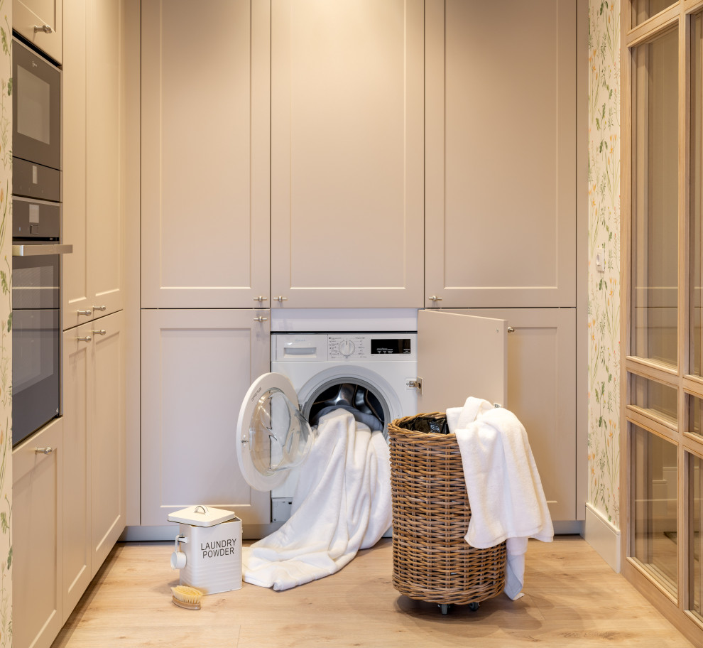 Inspiration for a mid-sized transitional l-shaped laundry cupboard in Bilbao with an undermount sink, raised-panel cabinets, grey cabinets, quartz benchtops, white splashback, engineered quartz splashback, multi-coloured walls, laminate floors, an integrated washer and dryer, brown floor, white benchtop, recessed and wallpaper.