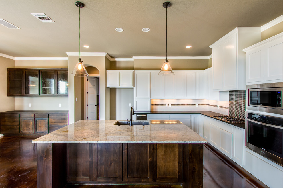 This is an example of a mid-sized traditional l-shaped open plan kitchen in Austin with a drop-in sink, flat-panel cabinets, white cabinets, granite benchtops, black splashback, subway tile splashback, stainless steel appliances, concrete floors and with island.