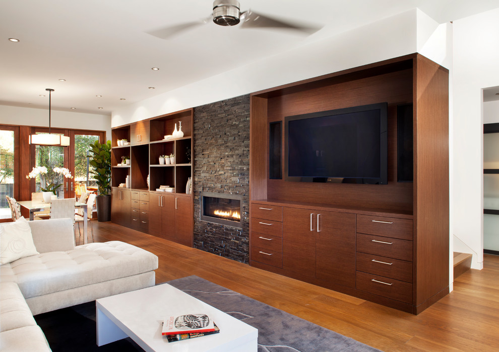 This is an example of a mid-sized contemporary open concept living room in San Francisco with white walls, medium hardwood floors, a standard fireplace, a stone fireplace surround, a wall-mounted tv and brown floor.