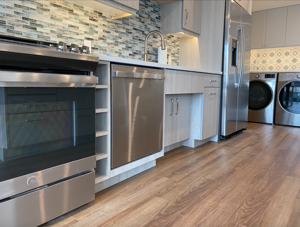 Medium sized traditional grey and white kitchen/diner in Philadelphia with a submerged sink, flat-panel cabinets, medium wood cabinets, engineered stone countertops, multi-coloured splashback, glass tiled splashback, stainless steel appliances, vinyl flooring, an island, brown floors and white worktops.