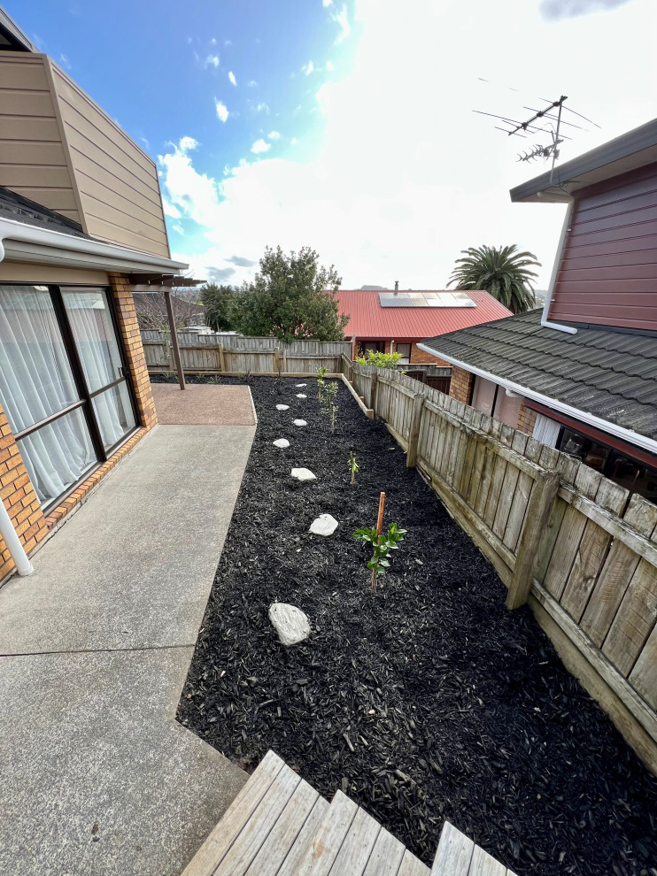 This is an example of a small tropical backyard formal garden for spring in Auckland with with raised garden bed, mulch and a wood fence.