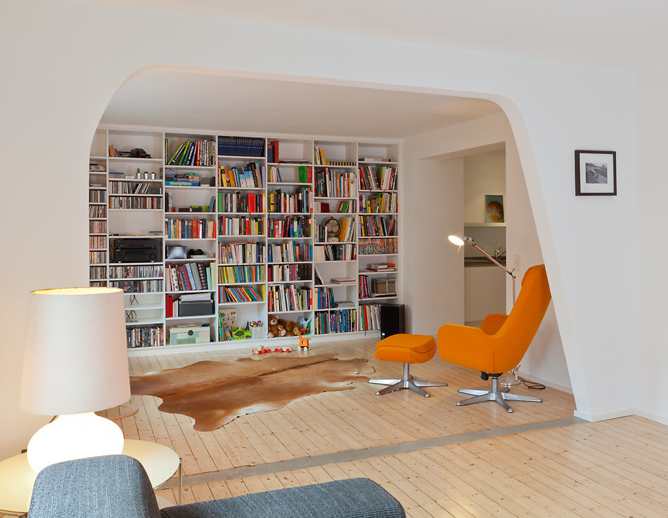 Small enclosed family room in Cologne with a library, white walls and light hardwood floors.