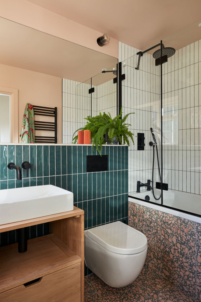 На фото: ванная комната в стиле модернизм с светлыми деревянными фасадами, накладной ванной, душем над ванной, инсталляцией, зеленой плиткой, розовыми стенами, полом из терраццо, тумбой под одну раковину и напольной тумбой