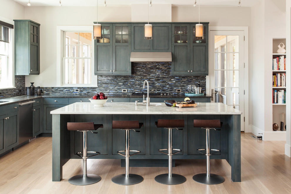 Photo of a large beach style l-shaped eat-in kitchen in Boston with an undermount sink, raised-panel cabinets, blue cabinets, marble benchtops, blue splashback, glass tile splashback, stainless steel appliances, light hardwood floors and with island.