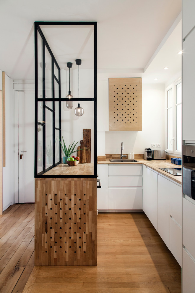 Inspiration for a mid-sized contemporary u-shaped eat-in kitchen in Paris with white cabinets, wood benchtops, timber splashback, a drop-in sink, flat-panel cabinets, brown splashback, panelled appliances, medium hardwood floors, a peninsula, brown floor and brown benchtop.