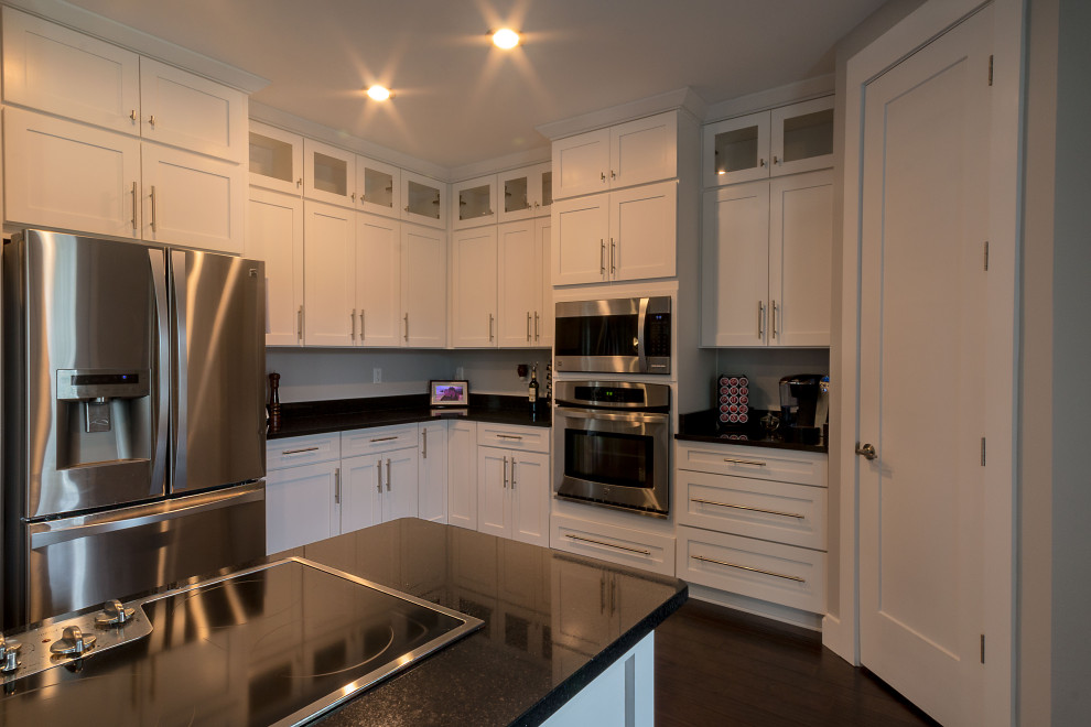 Example of a large l-shaped eat-in kitchen design with an undermount sink, shaker cabinets, white cabinets, granite countertops, an island and black countertops