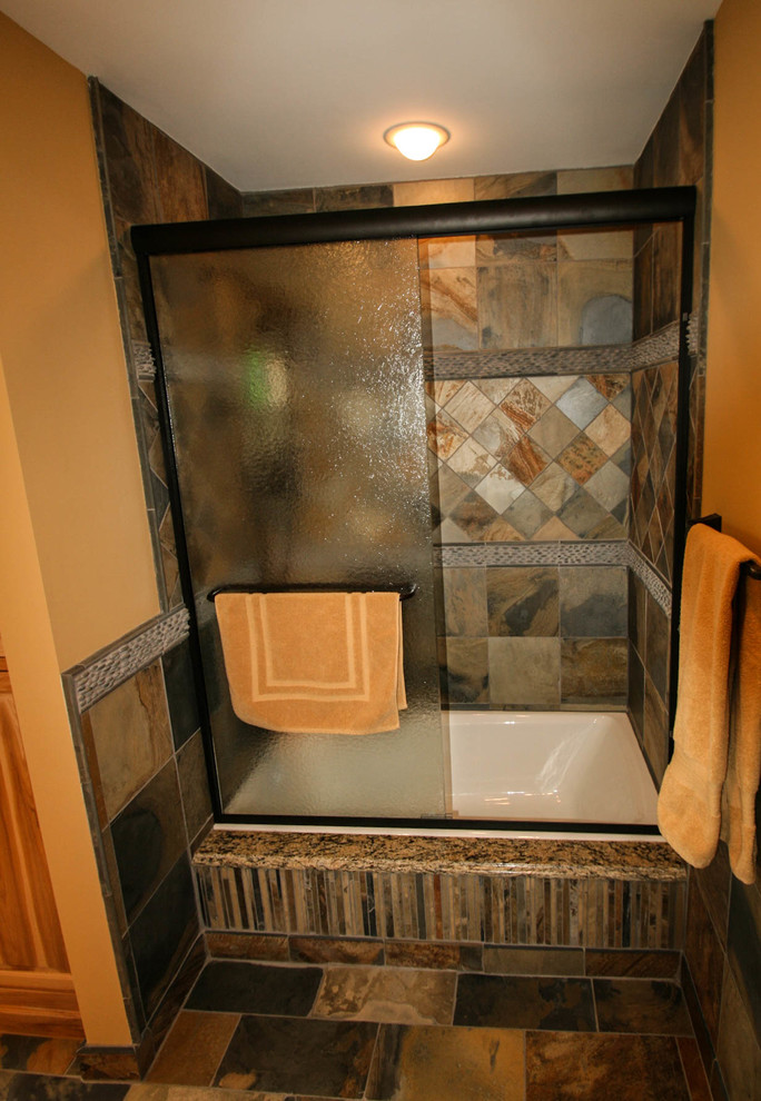 Photo of a mid-sized country kids bathroom in Minneapolis with an undermount sink, raised-panel cabinets, light wood cabinets, granite benchtops, a drop-in tub, a shower/bathtub combo, a two-piece toilet, multi-coloured tile, stone tile, yellow walls and slate floors.