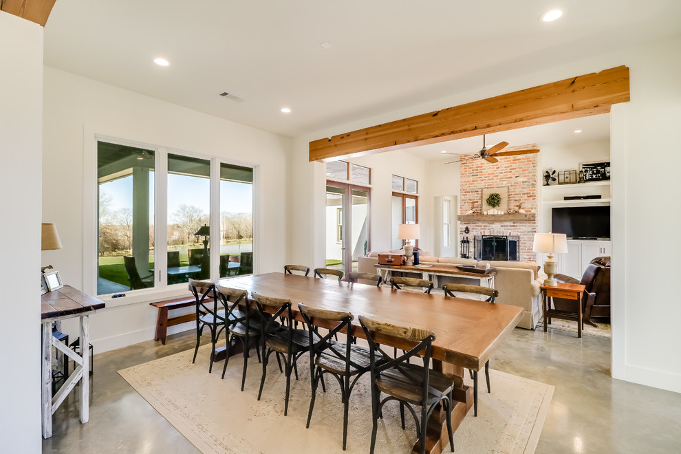 Design ideas for a large country open plan dining in Jackson with white walls, concrete floors, a standard fireplace, a brick fireplace surround and grey floor.