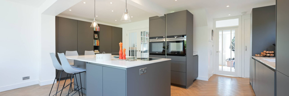 Photo of a large modern u-shaped open plan kitchen in Hertfordshire with an integrated sink, flat-panel cabinets, grey cabinets, quartzite benchtops, black appliances, with island, brown floor, white benchtop and recessed.