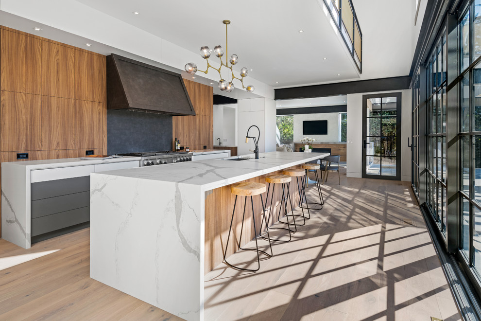 Inspiration for a contemporary galley kitchen in New York with an undermount sink, flat-panel cabinets, medium wood cabinets, stainless steel appliances, medium hardwood floors, with island, brown floor and white benchtop.