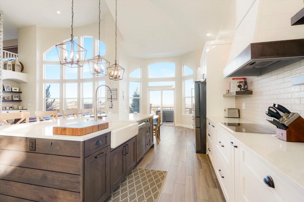 Photo of a large transitional single-wall open plan kitchen in Denver with a farmhouse sink, shaker cabinets, white cabinets, white splashback, subway tile splashback, black appliances, with island, white benchtop and vaulted.