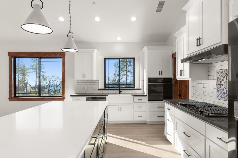 Example of a mid-sized farmhouse l-shaped light wood floor, brown floor and vaulted ceiling open concept kitchen design in Sacramento with shaker cabinets, white cabinets, granite countertops, white backsplash, subway tile backsplash, black appliances, an island and black countertops