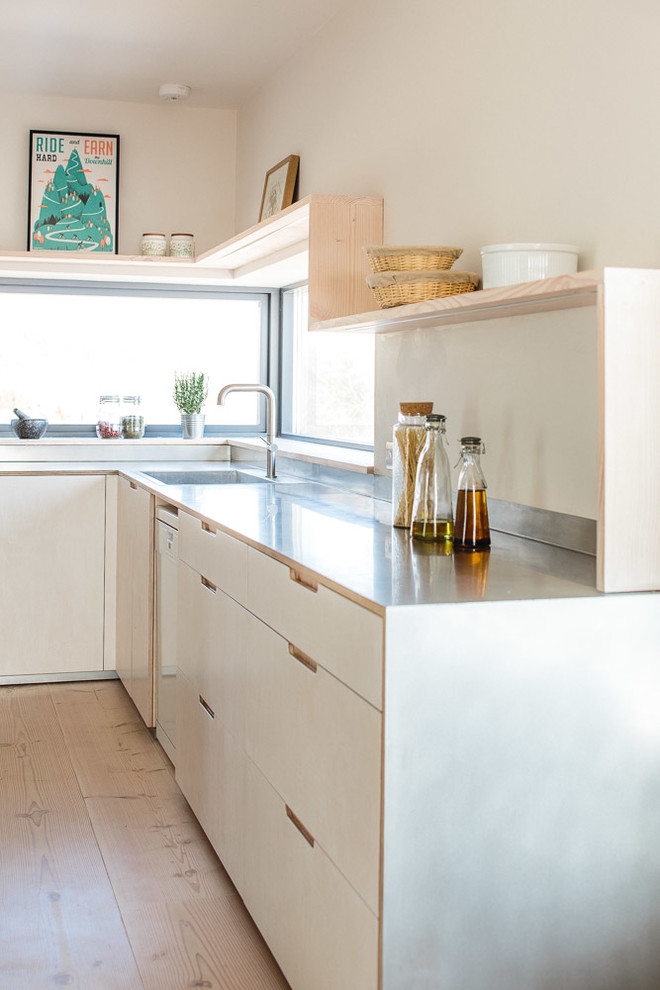 Mid-sized scandinavian l-shaped eat-in kitchen in Other with a farmhouse sink, flat-panel cabinets, light wood cabinets, stainless steel benchtops, metallic splashback, stainless steel appliances, light hardwood floors and with island.